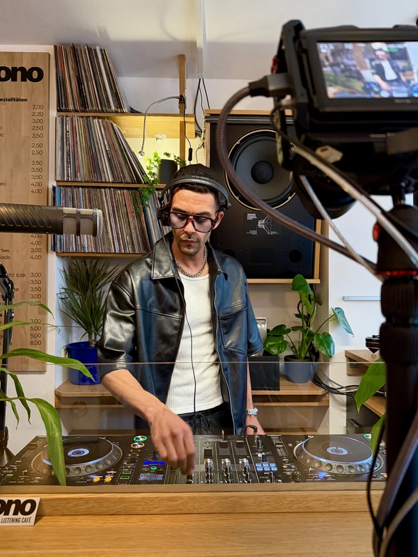 DJ JOK3R mixing in front of vinyl records and a camera